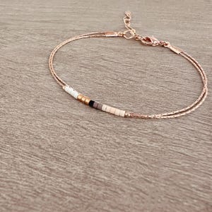 May include: A delicate double-strand bracelet with a small row of white, black, and brown beads.