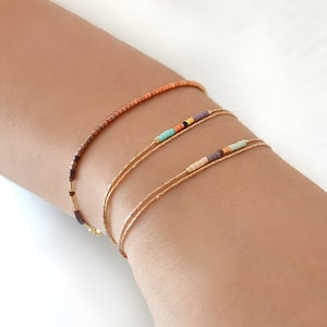 May include: Three gold chain bracelets with colorful beads. The top bracelet has brown beads, the middle bracelet has turquoise, orange, and black beads, and the bottom bracelet has purple, orange, and white beads.