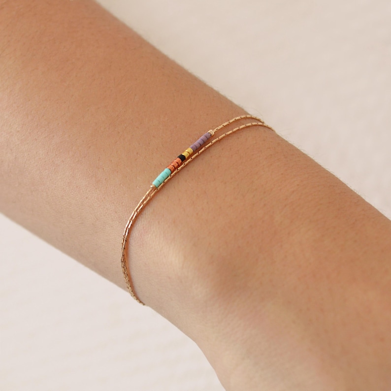 May include: A delicate gold chain bracelet with a colorful beaded accent. The beads are turquoise, orange, yellow, black, and purple.