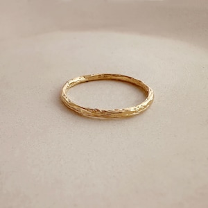Peut inclure: Une bague dorée à la surface texturée. La bague est circulaire et semble être en métal. La bague est posée sur un fond neutre.