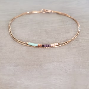 May include: A delicate gold chain bracelet with a row of colorful beads in shades of turquoise, purple, and pink.
