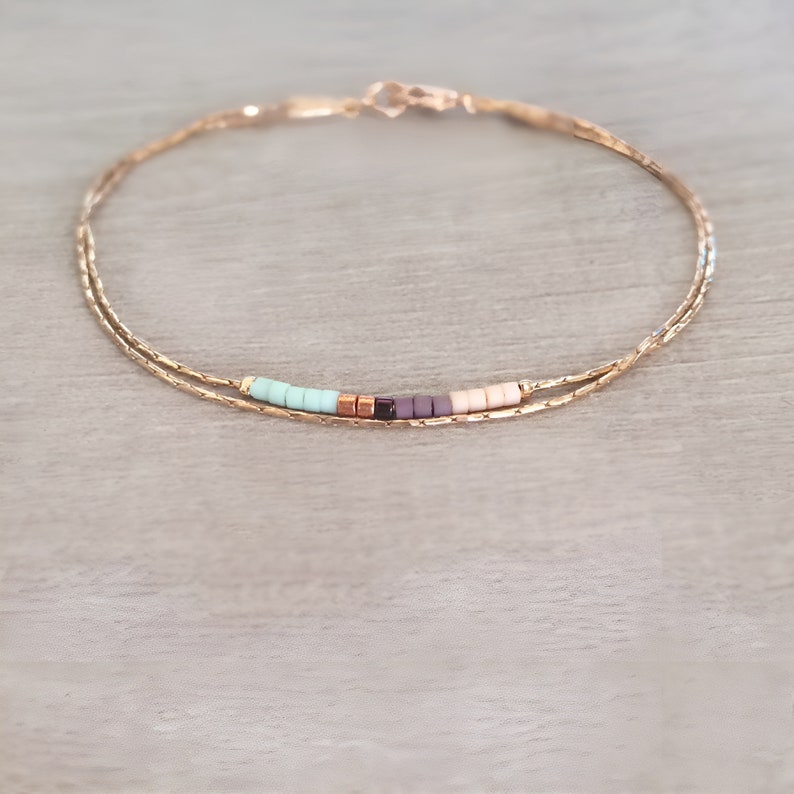 May include: A delicate gold chain bracelet with a row of colorful beads in shades of turquoise, purple, and pink.