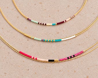 May include: Three delicate gold chain necklaces, each featuring a central segment of small, multicolored glass beads. The bead patterns include combinations of pink, turquoise, white, black, purple, and gold accents arranged in linear sequences.