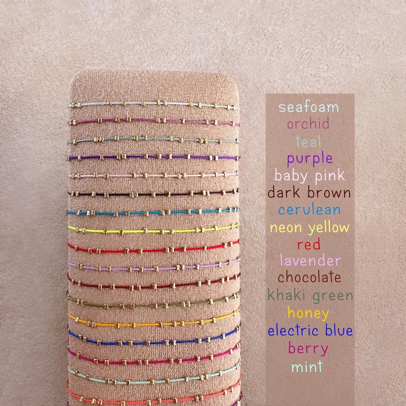 May include: A selection of colourful beaded bracelets in shades like seafoam, purple, and red. The bracelets are displayed on a neutral-toned stand, with a list of colour names visible on the right.