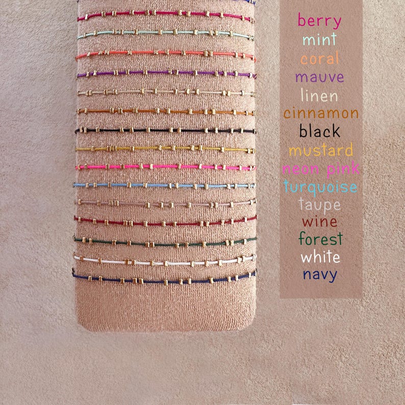 May include: A selection of beaded bracelets in shades like berry, mint, and coral, each with tiny gold beads. The bracelets are presented on a beige fabric. A colour chart lists the available colours, including turquoise and navy.