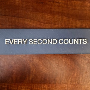 May include: A grey rectangular sign with the text "EVERY SECOND COUNTS" printed in white.