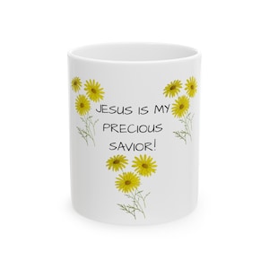 Puede incluir: Taza de cerámica blanca con un diseño floral de margaritas amarillas y el texto "¡Jesús es mi precioso salvador!"