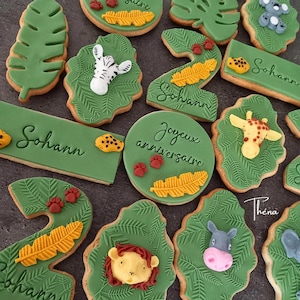 Peut inclure: Un assortiment de biscuits décorés sur le thème de la jungle avec du fondant vert texturé, des visages d'animaux comme un zèbre, un lion et une girafe, le chiffre deux, et des plaques rectangulaires avec le nom Sohann et Joyeux anniversaire.