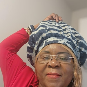 Puede incluir: Un boina a rayas azules y blancas se usa con una camiseta roja de manga larga. La boina est&aacute; hecha de una tela texturizada. La persona lleva gafas con montura dorada y un collar de oro.