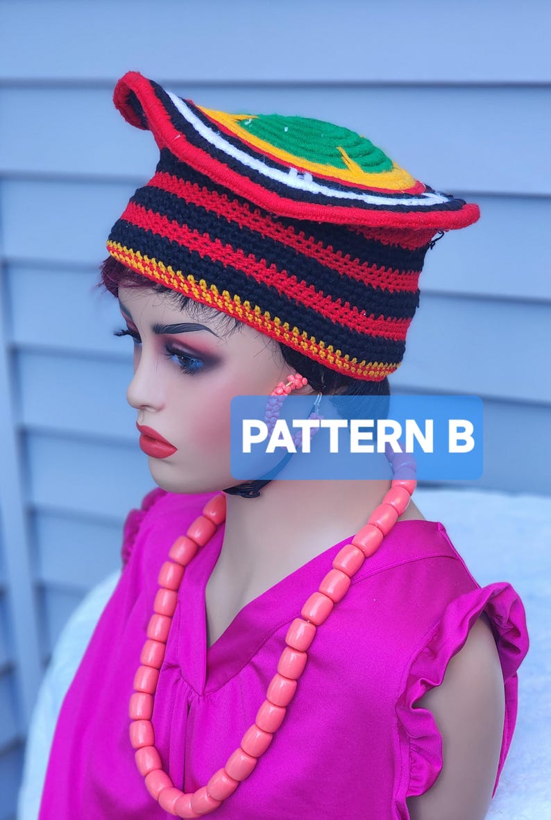 May include: A colorful, patterned hat with a curved brim, featuring red, black, white, yellow, and green stripes. The hat is worn by a mannequin, paired with a pink top and necklace. The text "PATTERN B" is visible.