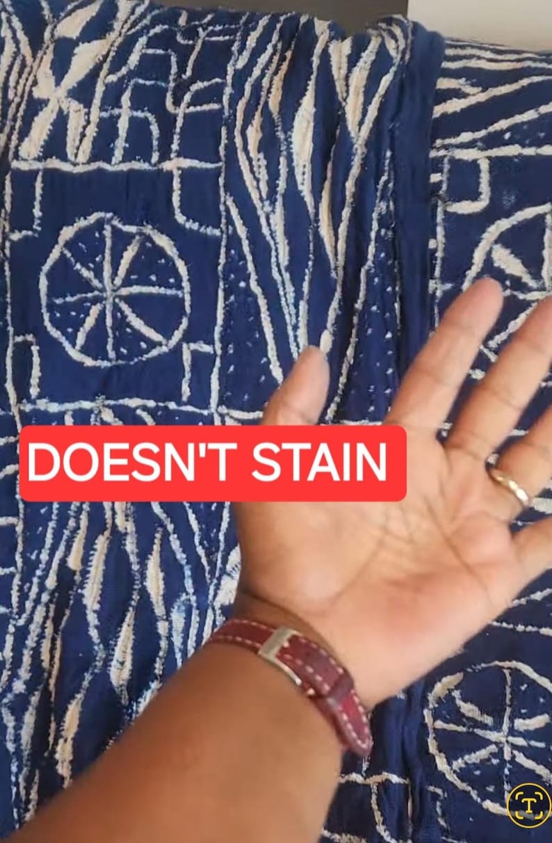 K&ouml;nnte beinhalten: Nahaufnahme eines blauen Stoffes mit wei&szlig;en abstrakten Mustern. Der Stoff hat ein sich wiederholendes Design mit kreisf&ouml;rmigen und linearen Elementen. Ein rotes Rechteck mit dem Text "DOESN'T STAIN" ist sichtbar. Ein Arm und eine Hand sind im Bild.