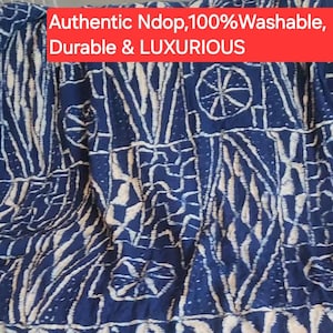 K&ouml;nnte beinhalten: Blau-wei&szlig; gemusterter Stoff mit Fransen am unteren Rand. Der Stoff weist ein sich wiederholendes Design aus geometrischen Formen und Linien auf. Der Text "Authentic Ndop, 100% Washable, Durable & LUXURIOUS" wird in einem roten Banner angezeigt.