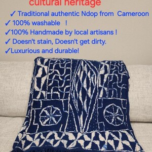 K&ouml;nnte beinhalten: Blau-wei&szlig;es Ndop-Textil aus Kamerun mit geometrischen Mustern und Fransen. Der Text lautet "NDOP: Kameruner Kulturerbe" und hebt seinen traditionellen und handgefertigten Charakter hervor.