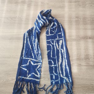 K&ouml;nnte beinhalten: Blauer Schal mit wei&szlig;en geometrischen Mustern und Fransen. Der Schal hat ein Sterndesign und vertikale Streifen. Der Schal besteht aus einem gewebten Stoff.