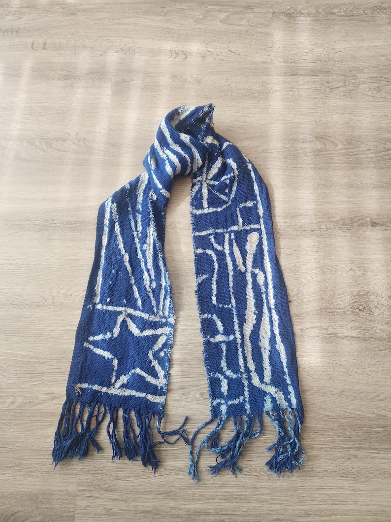 K&ouml;nnte beinhalten: Blauer Schal mit wei&szlig;en geometrischen Mustern und Fransen. Der Schal hat ein Sterndesign und vertikale Streifen. Der Schal besteht aus einem gewebten Stoff.