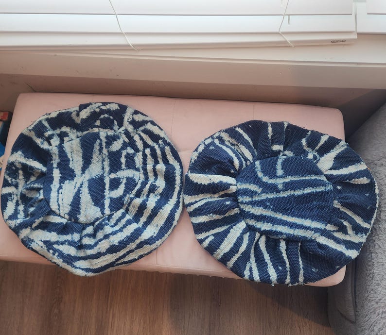 Puede incluir: Dos sombreros redondos de tela azul marino y blanca. Los sombreros tienen un aspecto texturizado con un dise&ntilde;o de l&iacute;neas blancas sobre un fondo azul marino. Los sombreros est&aacute;n colocados sobre una superficie rosa.