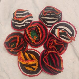 May include: A collection of handmade crochet hats. Each hat features a circular brim with a red border, and a striped pattern in black, white, and yellow. The interior of the hats reveals a mix of green, yellow, and red yarn.