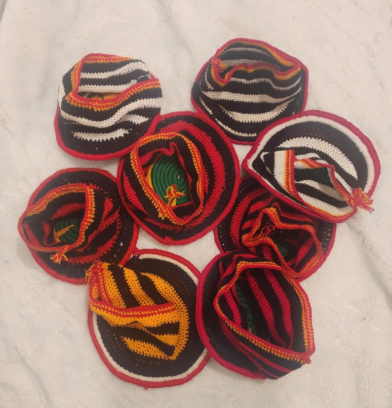 May include: A collection of handmade crochet hats. Each hat features a circular brim with a red border, and a striped pattern in black, white, and yellow. The interior of the hats reveals a mix of green, yellow, and red yarn.