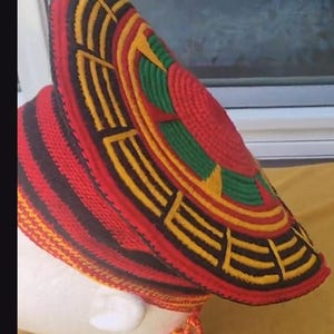 May include: A vibrant, handmade hat with a wide brim, featuring a striking pattern of red, black, yellow, and green. The hat has a unique, textured design and a tassel detail. This headwear is a bold statement piece.