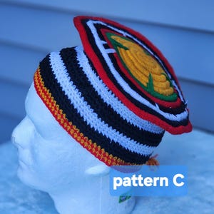 May include: A handmade crochet hat with a unique design. The hat features black and white stripes, a red and yellow trim, and a decorative top with a yellow and green emblem. The text "pattern C" is visible.