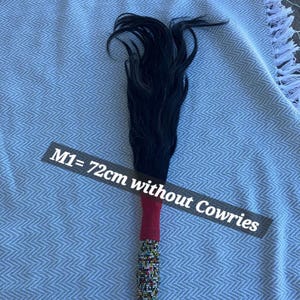 May include: A decorative item with a black, flowing top and a beaded handle. The handle is red and adorned with colorful beads. The text on the image reads "M1= 72cm without Cowries".