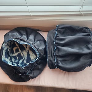 Puede incluir: Dos gorros de sat&eacute;n negro con interior estampado en azul y blanco. Un gorro est&aacute; abierto, revelando el dise&ntilde;o interior. El otro gorro est&aacute; cerrado. Los gorros est&aacute;n sobre una superficie rosa.