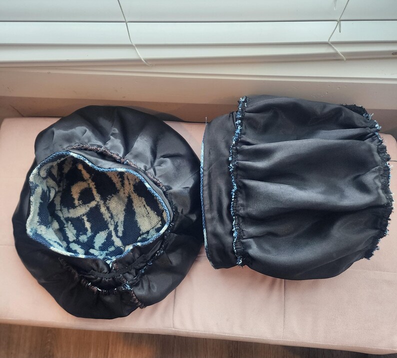 Puede incluir: Dos gorros de sat&eacute;n negro con interior estampado en azul y blanco. Un gorro est&aacute; abierto, revelando el dise&ntilde;o interior. El otro gorro est&aacute; cerrado. Los gorros est&aacute;n sobre una superficie rosa.