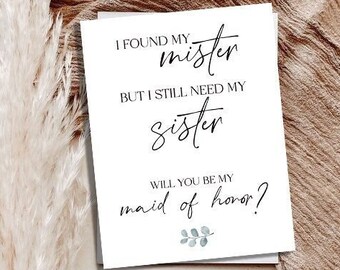 May include: A white card with black calligraphy that reads "I found my mister but I still need my sister. Will you be my maid of honor?" with a small green leaf illustration.