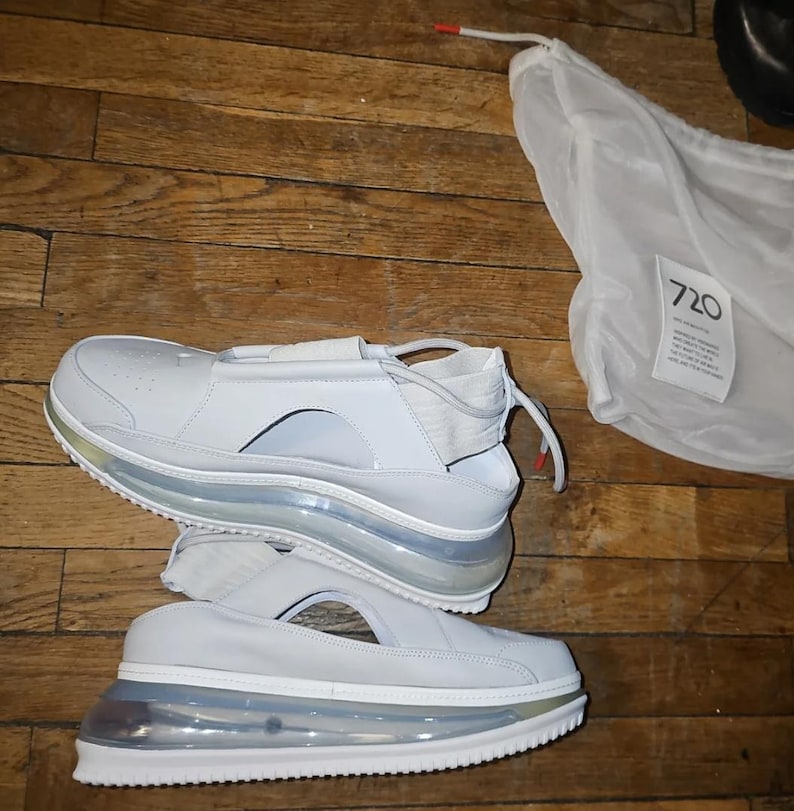 May include: White sneakers with a distinctive design, including a strap and cut-out detail. The soles are transparent, showcasing an air cushion. A white bag with the number "720" is also visible.