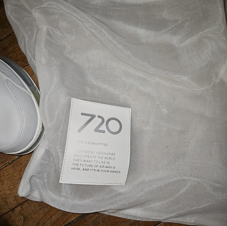 May include: A white trainer and a white fabric bag are visible. A white rectangular tag on the bag displays "720" and "NIKE AIR MAX FF720". The tag also includes text about visionaries and the future of Air Max.