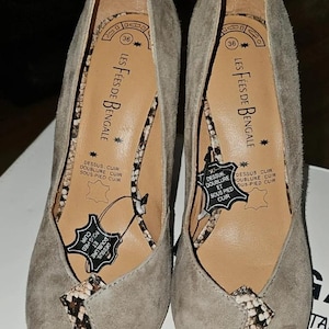 Peut inclure: Une paire d'escarpins en daim gris clair. Les chaussures ont un bout pointu et un motif peau de serpent sur l'empeigne. L'intérieur de la chaussure porte la mention "LES FÉES DE BENGALE". Taille 36.