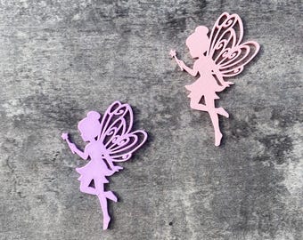 Può includere: Due ritagli di fata in rosa e lavanda, ciascuno con intricati disegni alari e una bacchetta. Le fate sono in posa di volo, con le gambe distese. Lo sfondo è una superficie grigia strutturata.