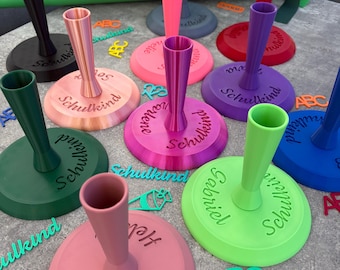 May include: A collection of colorful, circular plastic candle holders with a central stem, each featuring the embossed German word Schulkind. The set includes various bright colors like pink, green, purple, blue, and black, accompanied by small cutout letters and numbers scattered on the surface.