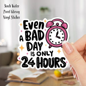 Puede incluir: Un despertador rosa con una cara blanca y agujas negras est&aacute; rodeado de estrellas. El texto "Even a bad day is only 24 hours" est&aacute; escrito en letras negras.