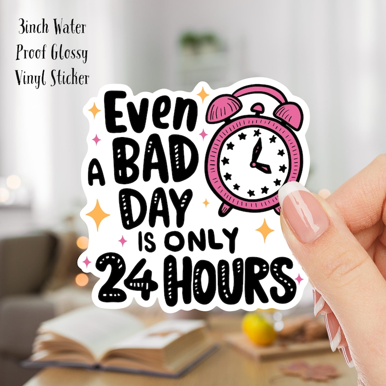 Puede incluir: Un despertador rosa con una cara blanca y agujas negras est&aacute; rodeado de estrellas. El texto "Even a bad day is only 24 hours" est&aacute; escrito en letras negras.