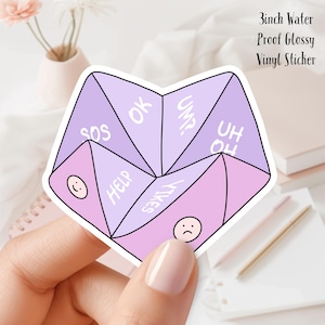 May include: A glossy vinyl sticker in a fortune teller design, featuring shades of purple and pink. The sticker has phrases like "SOS," "OK," and "YIKES," along with two smiley faces. The text "3inch Water Proof Glossy Vinyl Sticker" is also included.