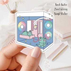 Puede incluir: Una pegatina de vinilo brillante impermeable de 7,6 cm que presenta una ilustración de dibujos animados de una caja de computadora con dos ranas adentro. La caja de la computadora tiene un esquema de color rosa y azul con ventiladores de colores arcoíris. La pegatina tiene un borde blanco.