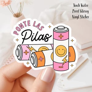May include: A 3-inch water-proof glossy vinyl sticker featuring three cartoon batteries in pink, orange, and white. The sticker has the phrase "Ponte Las Pilas" in pink and black lettering, with a smiley face and lightning bolt graphic.