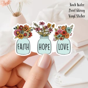 Op de afbeelding: Drie 7,6 cm waterdichte, glanzende vinyl stickers met glazen potten gevuld met kleurrijke bloemen en de woorden "Geloof", "Hoop" en "Liefde".