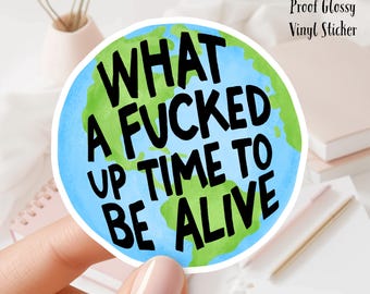 May include: A 3 inch water-proof glossy vinyl sticker with a blue and green watercolor illustration of the Earth. The sticker features the text "What a fucked up time to be alive".
