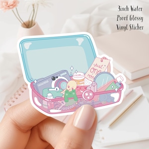May include: A 3 inch waterproof glossy vinyl sticker featuring a pink and blue open suitcase filled with various items including a camera, a frog, a baby doll, a bottle of lotion, a book, and a mirror. The text "Just One More" is visible on the book.