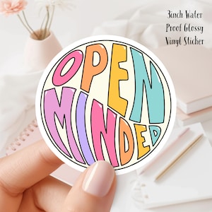 May include: A round, glossy vinyl sticker with the words "OPEN MINDED" in a colorful, retro font. The text is in pink, orange, yellow, and teal, set against a cream background. The sticker is 3 inches in diameter.