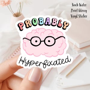 May include: A 3 inch water-proof glossy vinyl sticker with a pink brain wearing glasses and the text "Probably Hyperfixated" in rainbow colours.