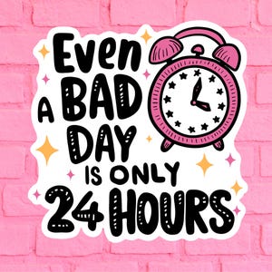 Puede incluir: Pegatina blanca con texto negro que dice "Incluso un mal d&iacute;a solo tiene 24 horas". Un despertador rosa con manecillas negras y estrellas negras alrededor de la esfera del reloj est&aacute; a la derecha del texto.