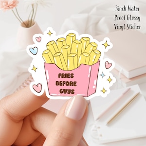 Może przedstawiać: Naklejka winylowa o wymiarach 7,6 cm, wodoodporna, z błyszczącym wykończeniem, przedstawiająca kreskówkową ilustrację frytek w różowym pudełku w kolorze różowym i żółtym. Tekst "FRIES BEFORE GUYS" jest napisany brązowym kolorem na pudełku.