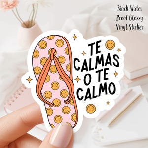 Könnte beinhalten: Ein glänzender Vinyl-Aufkleber mit einem rosa Flip-Flop-Design, verziert mit gelben Smiley-Gesichtern. Der Aufkleber hat orangefarbene Riemen und den Text "TE CALMAS O TE CALMO" in Schwarz. Der Aufkleber ist 7.6 cm groß.