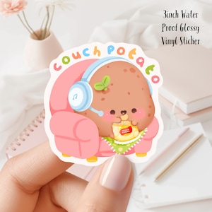 Puede incluir: Una pegatina de vinilo brillante impermeable de 7,6 cm que presenta una patata de dibujos animados con auriculares y sentada en un sofá rosa, comiendo patatas fritas. La pegatina dice "Couch Potato" en letras de colores.