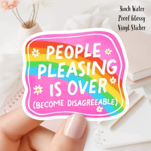 May include: A pink sticker with a rainbow and the text "*PEOPLE* PLEASASING *IS OVER* (BECOME DISAGREEABLE)". The sticker is 3 inches in diameter.