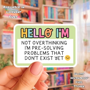 Op de afbeelding: Een rechthoekige sticker met de tekst "HELLO I'M NOT OVERTHINKING I'M PRE-SOLVING PROBLEMS THAT DON'T EXIST YET" in zwart, roze, oranje en blauw. De sticker is wit met een lichtgroene rand en een gele smiley. De sticker is glanzend, waterdicht en vinyl.