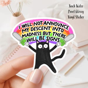May include: A black cat sticker with the text "I WILL NOT ANNOUNCE MY DESCENT INTO MADNESS BUT THERE WILL BE SIGNS" above the cat. The cat is holding two toy chainsaws. The sticker is 3 inches and water proof.